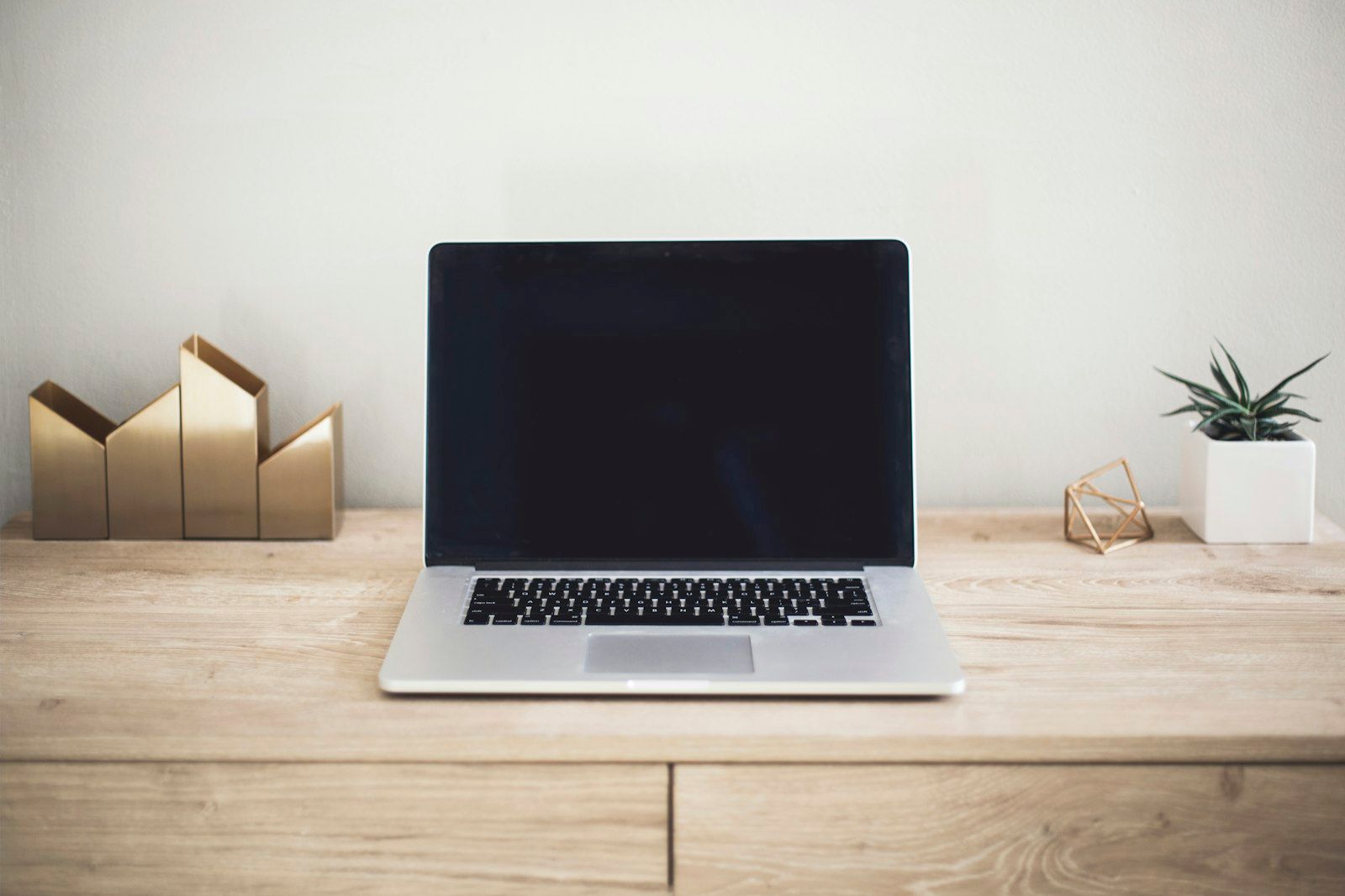 A closed MacBook Pro on a clean wooden desk — the workday the glasses plug into
